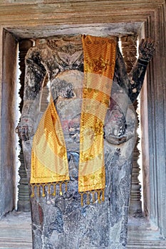 An ancient decapitated stone sculpture of Buddha in a Cambodian temple decorated with yellow robes