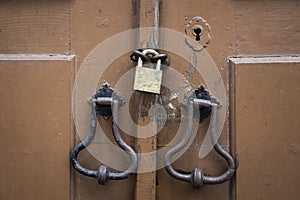 Ancient door knockers, lock and a padlock of an ancient brown wooden door