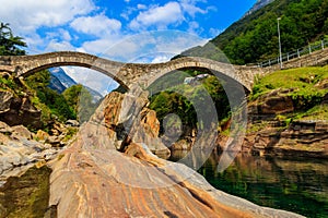Ancient double arch stone Roman bridge (Ponte dei Salti) over clear water of the Verzasca river