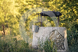 Ancient draw-well in European village, Old Water Well With Pulley and Bucket, Moldova, Green grass and trees. Sunny day. sunset