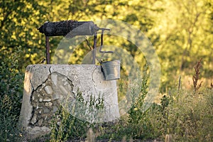 Ancient draw-well in European village, Old Water Well With Pulley and Bucket, Moldova, Green grass and trees. Sunny day. sunset