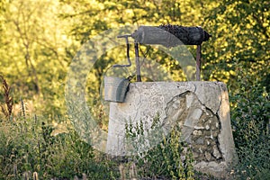 Ancient draw-well in European village, Old Water Well With Pulley and Bucket, Moldova, Green grass and trees. Sunny day. sunset