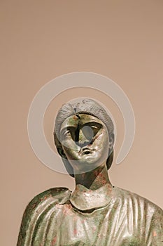 Ancient Greek brass sculpture of woman with a bashed in face against tan background - room for copy photo