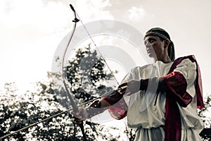 Ancient greek woman archer aims and shoots from bow on meadow