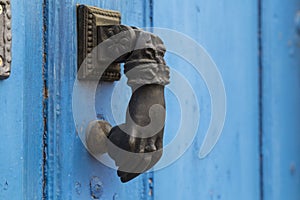 Ancient hand-shaped knob to knock on an old wooden blue door