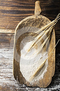 Ancient handmade rustic wooden scoop for flour with wheat ears on a dark natural wooden background. The concept of a