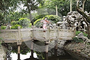 Ancient historic Asian Chinese woman artist traditional chi-pao cheongsam in a garden play musical instruments violin on bridge