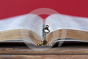 Ancient key in front of an open Holy Bible Book with golden pages on a wooden table, copy space