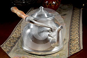 Ancient metallic teapot with wooden handle on an embroidered mat