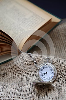 ancient pocket watch in front of an old book on a piece of cloth