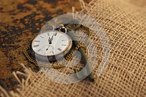 Ancient pocket watch and key on old folio half-covered with old sackcloth. Time passing concept. Knowledge eternity concept