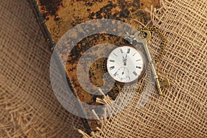 Ancient pocket watch and key on old folio half-covered with old sackcloth. Time passing concept. Knowledge eternity concept