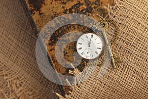 Ancient pocket watch and key on old folio half-covered with old sackcloth. Time passing concept. Knowledge eternity concept photo