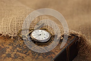 Ancient pocket watch and key on old folio half-covered with old sackcloth. Time passing concept. Knowledge eternity concept