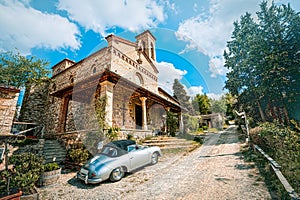 An ancient Porsche is parked outside of a countryside church in the Tuscan hills of Chianti, between Pisa and Florence