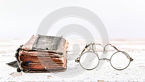 Ancient prayer book with old spectacles on the wooden table, view at an angle, banner with space for text