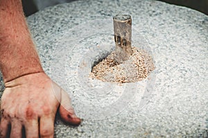 The ancient quern stone hand mill with grain close up. The man grinds the grain into flour with the help of a millstone