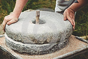 The ancient quern stone hand mill with grain. The man grinds the grain into flour with the help of a millstone. Men`s photo