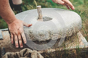 The ancient quern stone hand mill with grain. The man grinds the grain into flour with the help of a millstone. Men`s