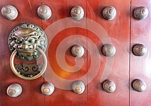 Ancient red wooden door decorated with bronze casting bas relief into Chinese lion face holding a ring-shaped handle in the mouth