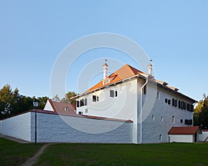 Ancient restored white stone building with red roof against blue sky background.