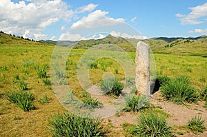 An ancient ritual stone stands in a valley at the foot of a mountain range