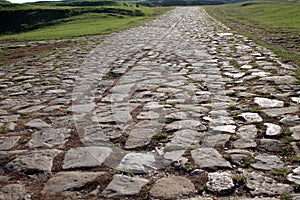 Ancient road paved with cobblestone and going up through hills.