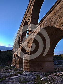 Ancient Roman aqueduct Pont du Gard with majestic stone arches above Gardon river after sunset near Vers-Pont-du-Gard, France.