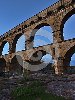 Ancient Roman aqueduct Pont du Gard with stone pillars above Gardon river after sunset near Vers-Pont-du-Gard, Occitanie, France.