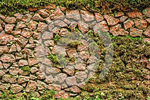 Ancient rough cobble stone wall with moss textured. Granite rocks, green moss