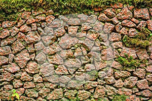 Ancient rough cobble stone wall with moss textured. Granite rocks, green moss