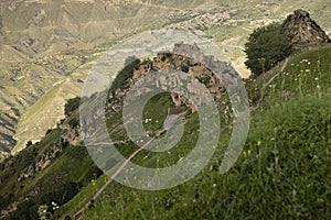 Ancient ruin of stone impregnable city on peak of mountain with road in highlands in Dagestan with landscape - green slopes, deep.