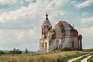 Ancient ruined Russian church or temple overgrown with grass among field