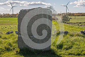 Ancient runestone with wind power on the background in a landscape at the swedish island Oland in the Baltic Sea