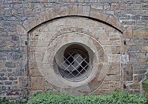 Ancient sandstone wall with arch and barred round window