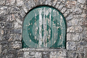 Ancient semicircular window with nailed green wooden shutters.