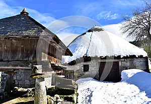 Ancient snowy palloza house and wooden horreo granary galician granary. Piornedo, Ancares, Galicia, Spain. photo