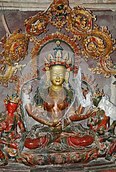 An ancient statue of a female Tibetan deity with a bronze-colored face and four arms in a monastery