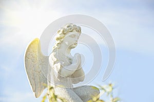 Ancient statue of little guards angel in flowers and  in the sunlight. Love, faith, hope, religion, Christianity, good concept