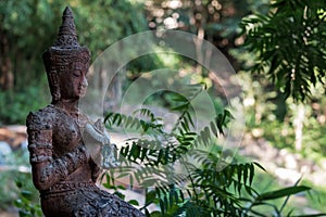 An ancient statue of a meditating buddha against a backdrop of a green forest or jungle.