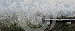 Ancient stone bench in front of old gray wall with crumbling plaster and green moss. Narrow vintage background