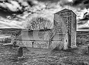 Ancient stone church is situated adjacent to a road on a somber, overcast day