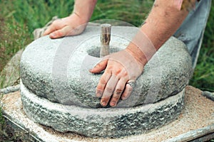 The ancient stone hand grain mill. Men`s hands rotate a stone millstone photo