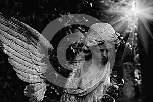 Ancient stone statue of angel of death in sun rays. Black and white image