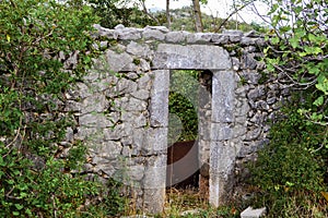 An ancient stone wall of a ruined house with a door among the grass. Old house, ruins, background