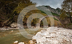 Ancient, stoned , arched bridge on the Portaikos river in autumn. Trikalla pyli village Thessaly Greece