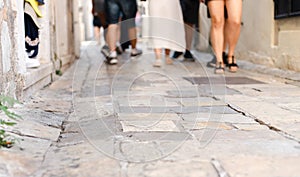 An ancient street paved with stone and blured legs of tourists in the background. Tour of the old city. Vacation and travel