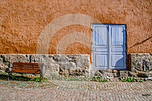 An ancient textured wall with a stone basement, a blue door and a bench.