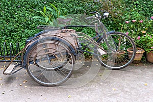 Ancient Tricycle bicycle antique and vintage with parking at green fence background. Local Tricycle bicycle Asian style Thailan