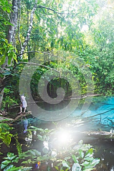 Ancient turquoise pond in tropical forest. Sunbeam shines through the branches of trees on the pond and lush foliage. Tourist